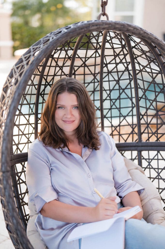 online CEO mentor brand photoshoot for taylor lee at her Florida home in egg chair writing in a notebook wearing a lavender top