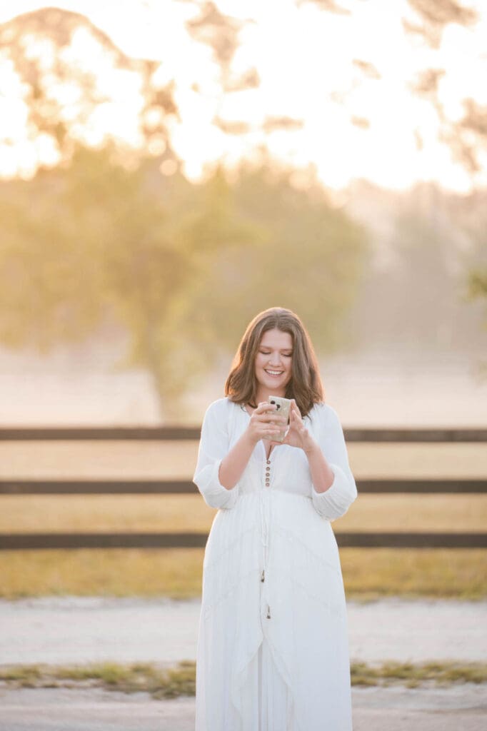 female entrepreneur business coach taylor lee texting clients on a walk at her farm while wearing a white dress