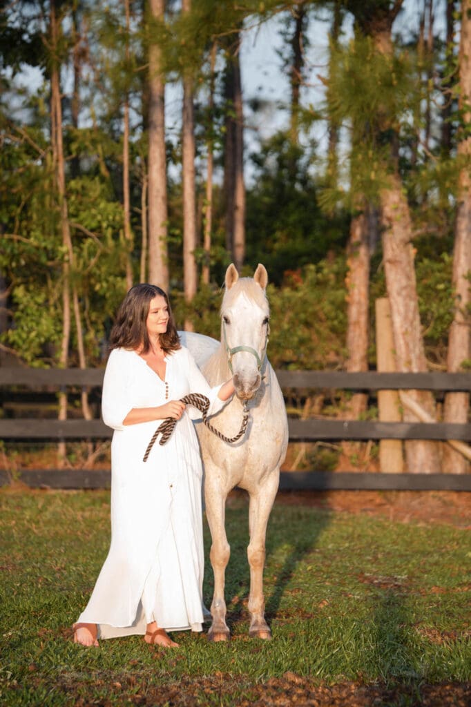 high ticket business coach taylor lee in a dress walking her white horse on her Florida farm