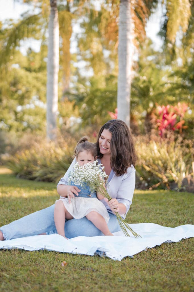 brand photography for female business coach taylor lee balancing business and motherhood sitting in the grass with her daughter playing with flowers