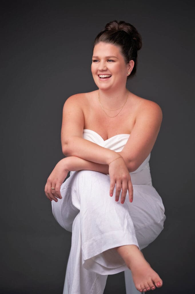coaching funnel branding photos for taylor lee sitting on stool on dark grey wearing white jumpsuit